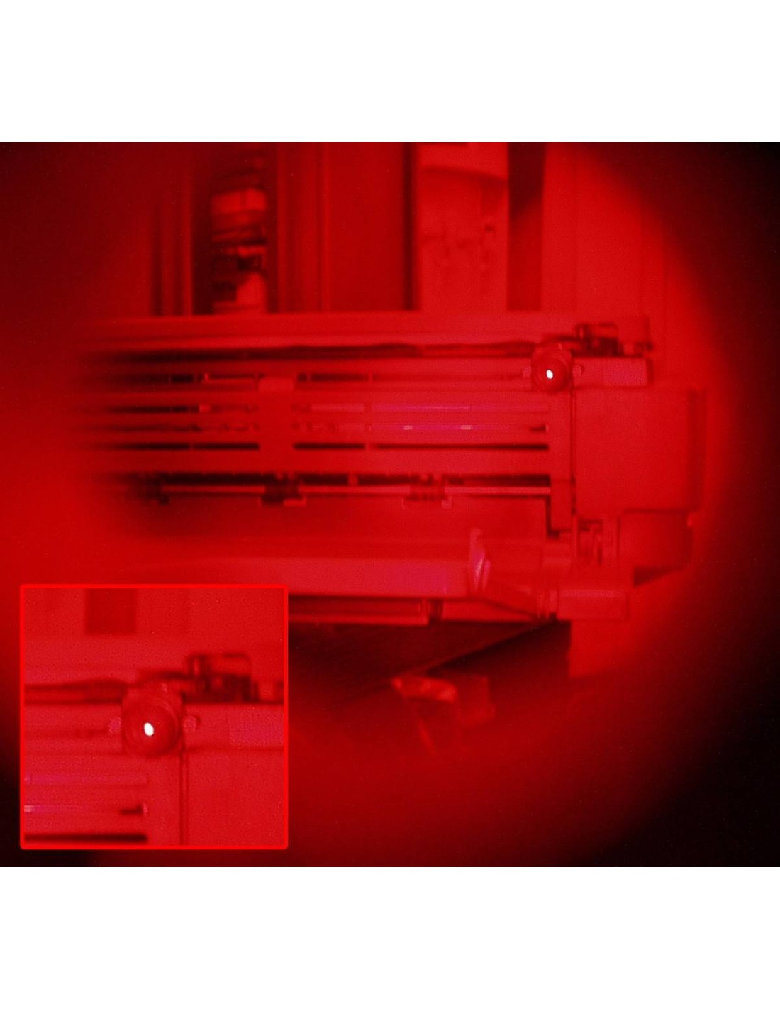 Câble et boitier d’équipement de surveillance vus sous lumière rouge, avec un petit objectif rouge brillant en premier plan.